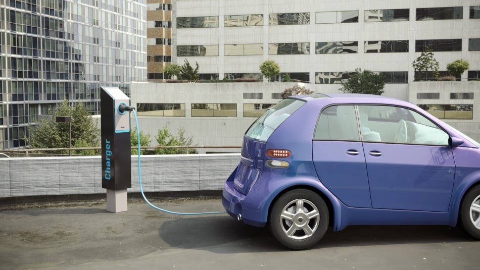A blue car is parked on a city street plugged into an electric vehicle charging station
