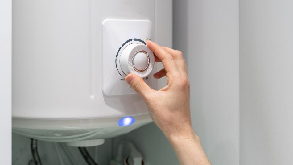 A closeup of a person’s hand adjusting the temperature control on an electric water heater