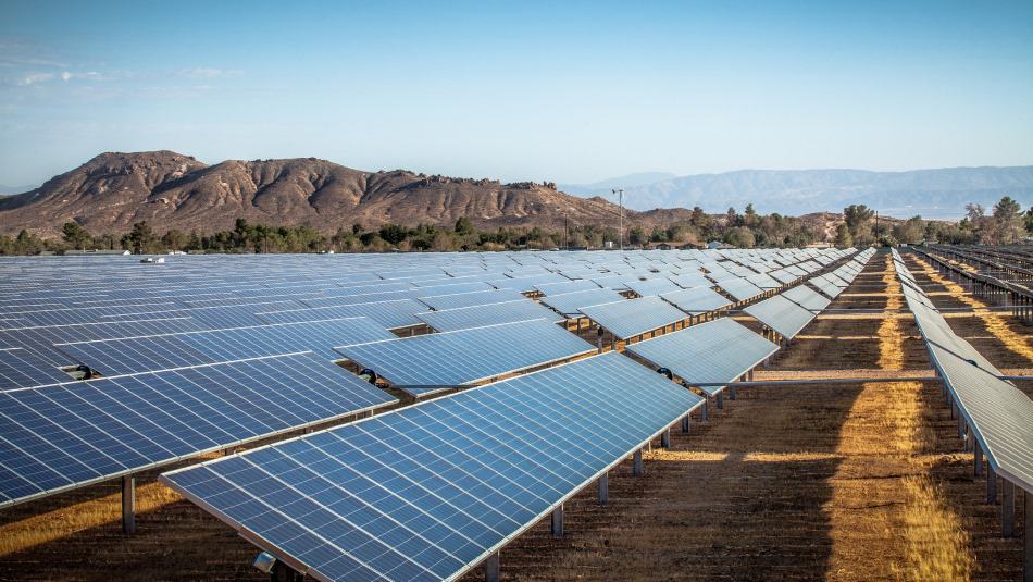 A field of solar panels in Rosamond, CA sits in front of two distant sets of mountains